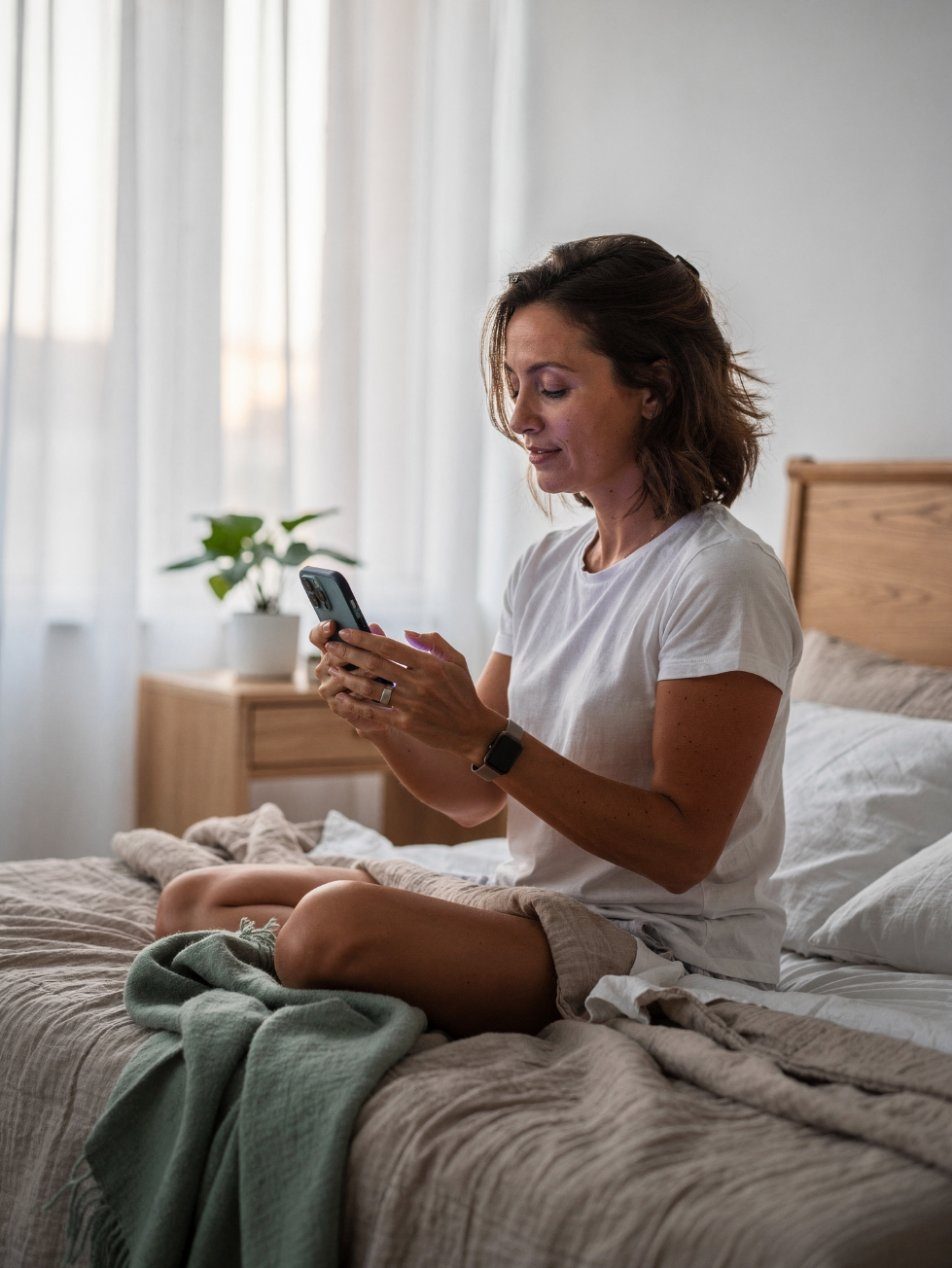 A woman sitting on her bed in the morning, checking her phone